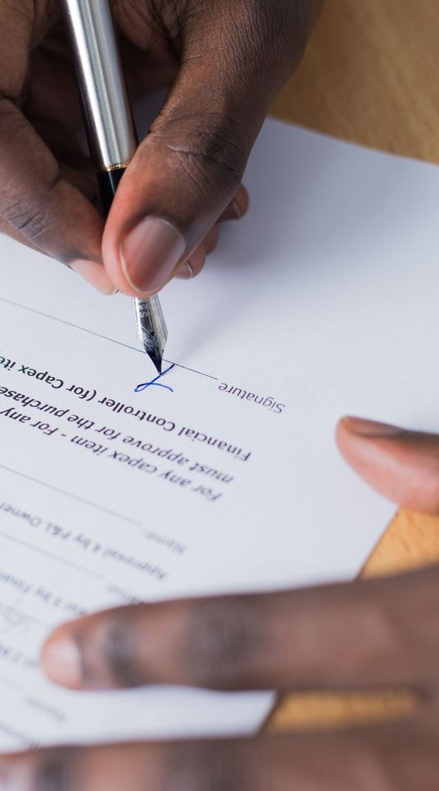 A hand signing a printed agreement with a pen