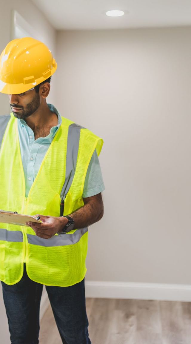Inspector in a hard hat and hi-vis vest checking a window in a finished room