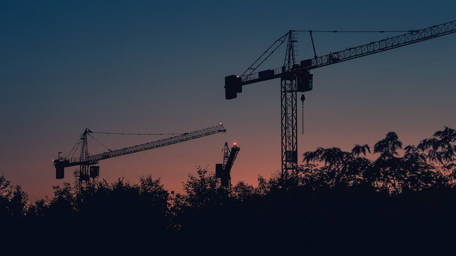 Tower cranes silhouetted against the sky at dusk