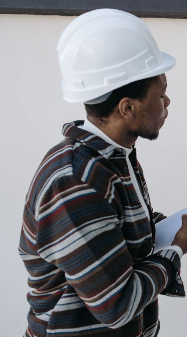 A man in a hard hat checking a wall with a spirit level, drawings in hand
