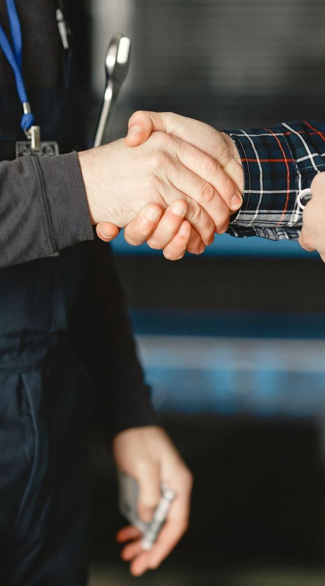 A tradesperson in work overalls, wrench in hand, shaking hands with a customer