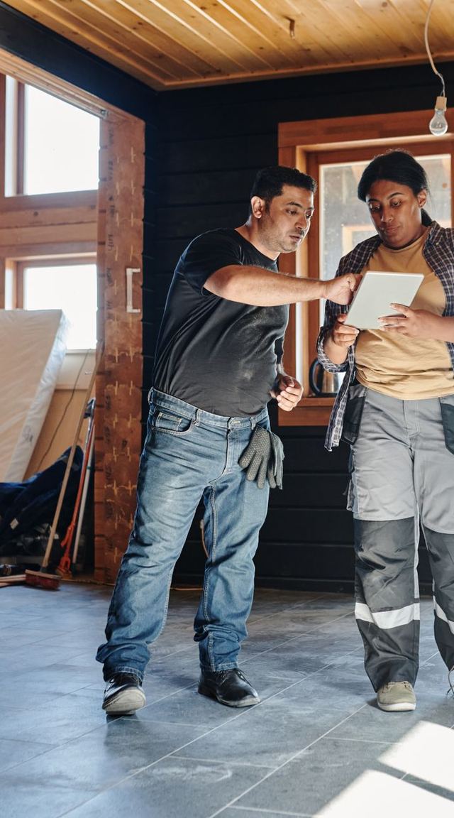 Two people reviewing a tablet inside a house under renovation
