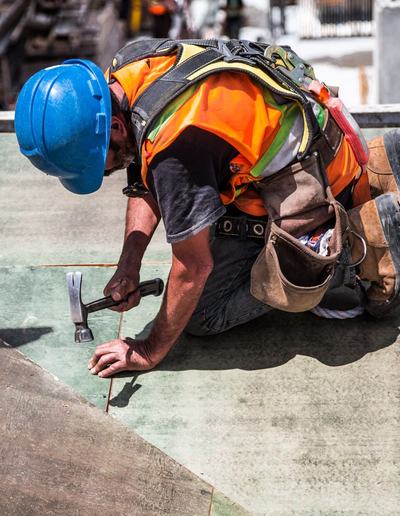 Roofer in a hard hat and harness hammering on a roof deck