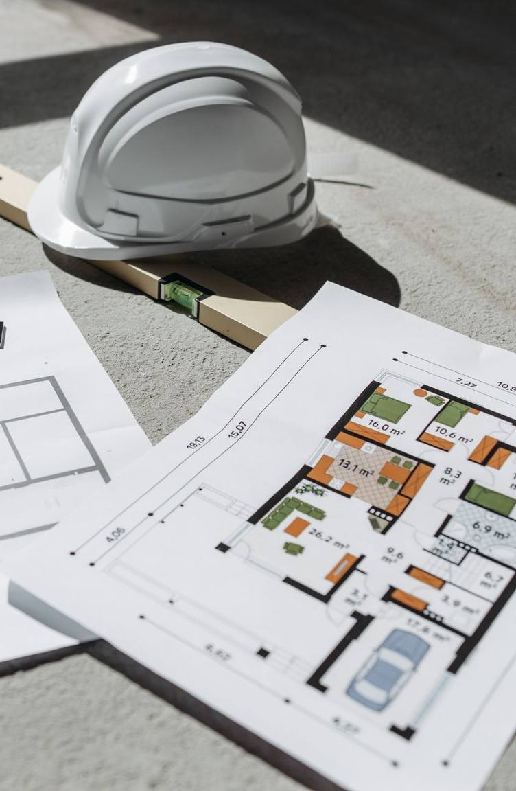 Floor plans, a spirit level and a hard hat lying on a concrete slab