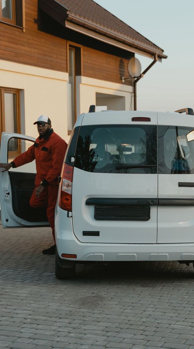 A tradesperson getting out of a work van in front of a house
